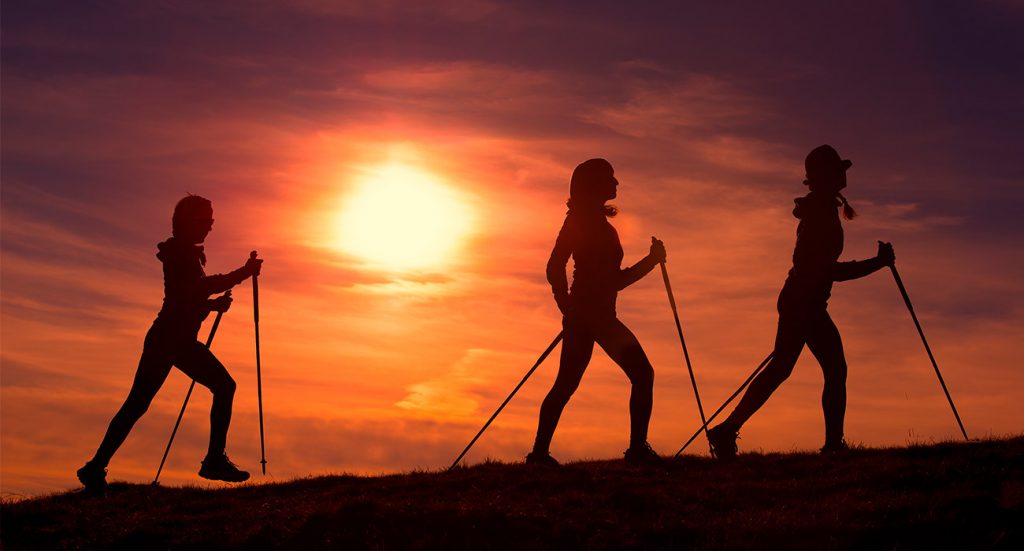 Tres mujeres practicando marcha nórdica en la montaña al atardecer | Sevilla Senior